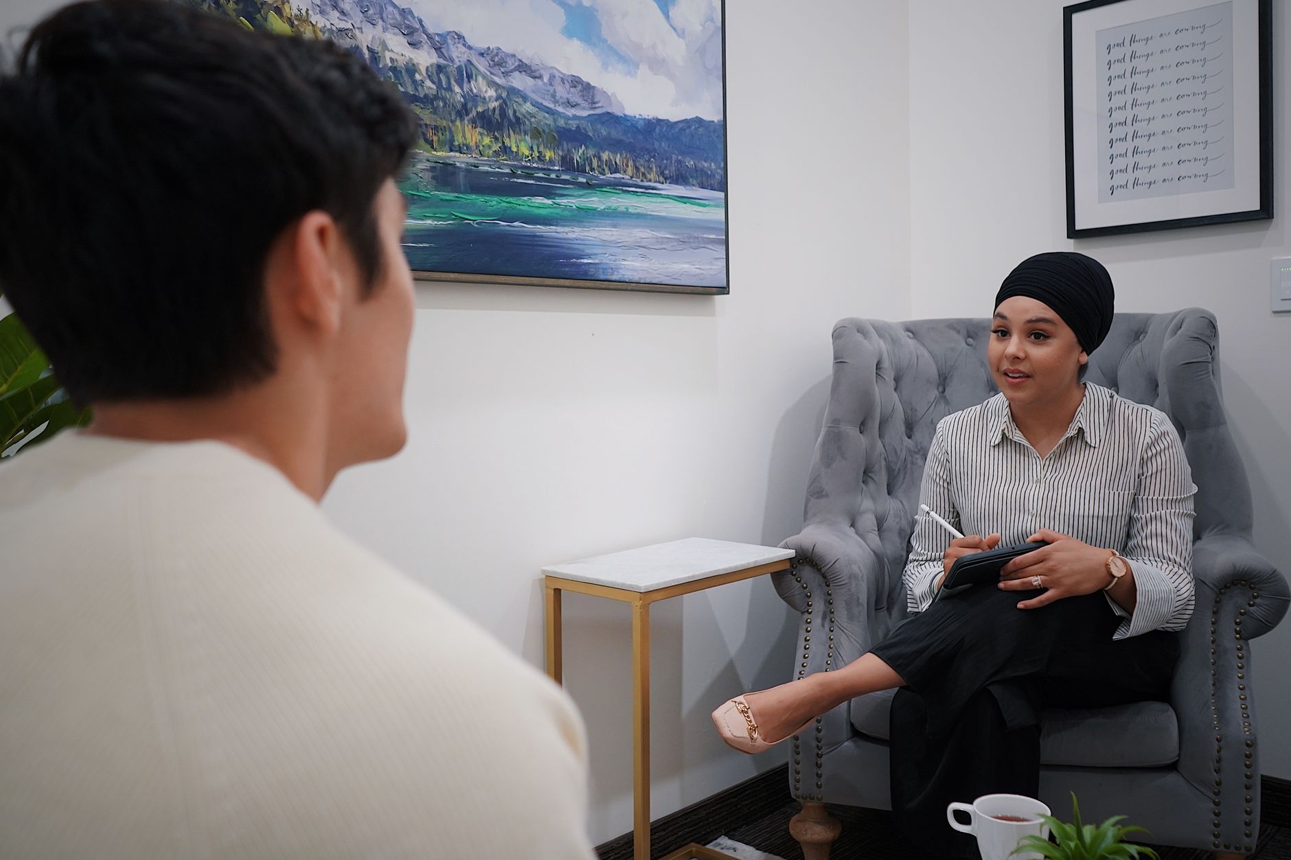 Person sitting in a comfortable chair talking to a therapist in a calm office with a notepad and tissues