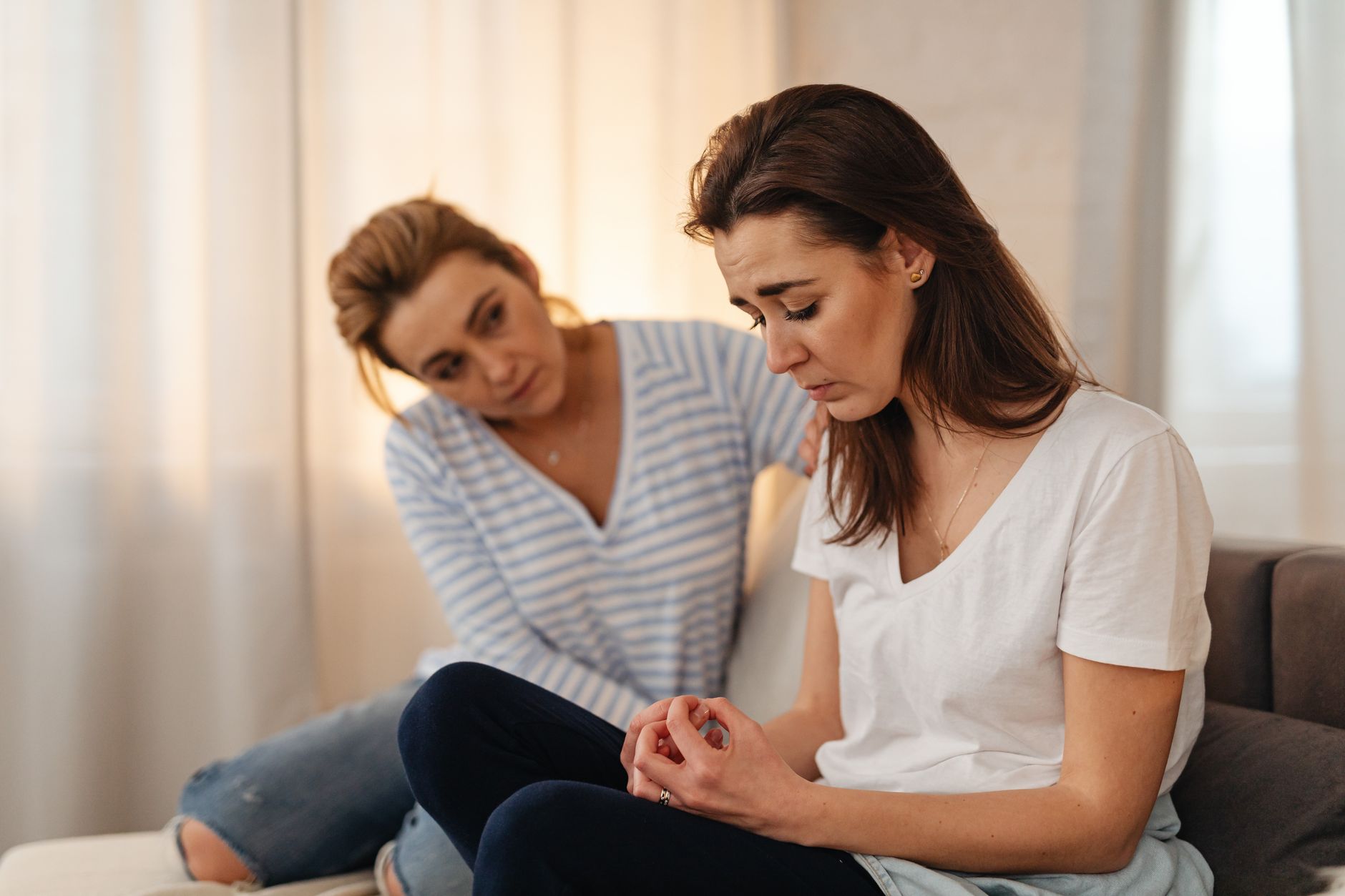 One person comforting a friend on a couch during a serious conversation
