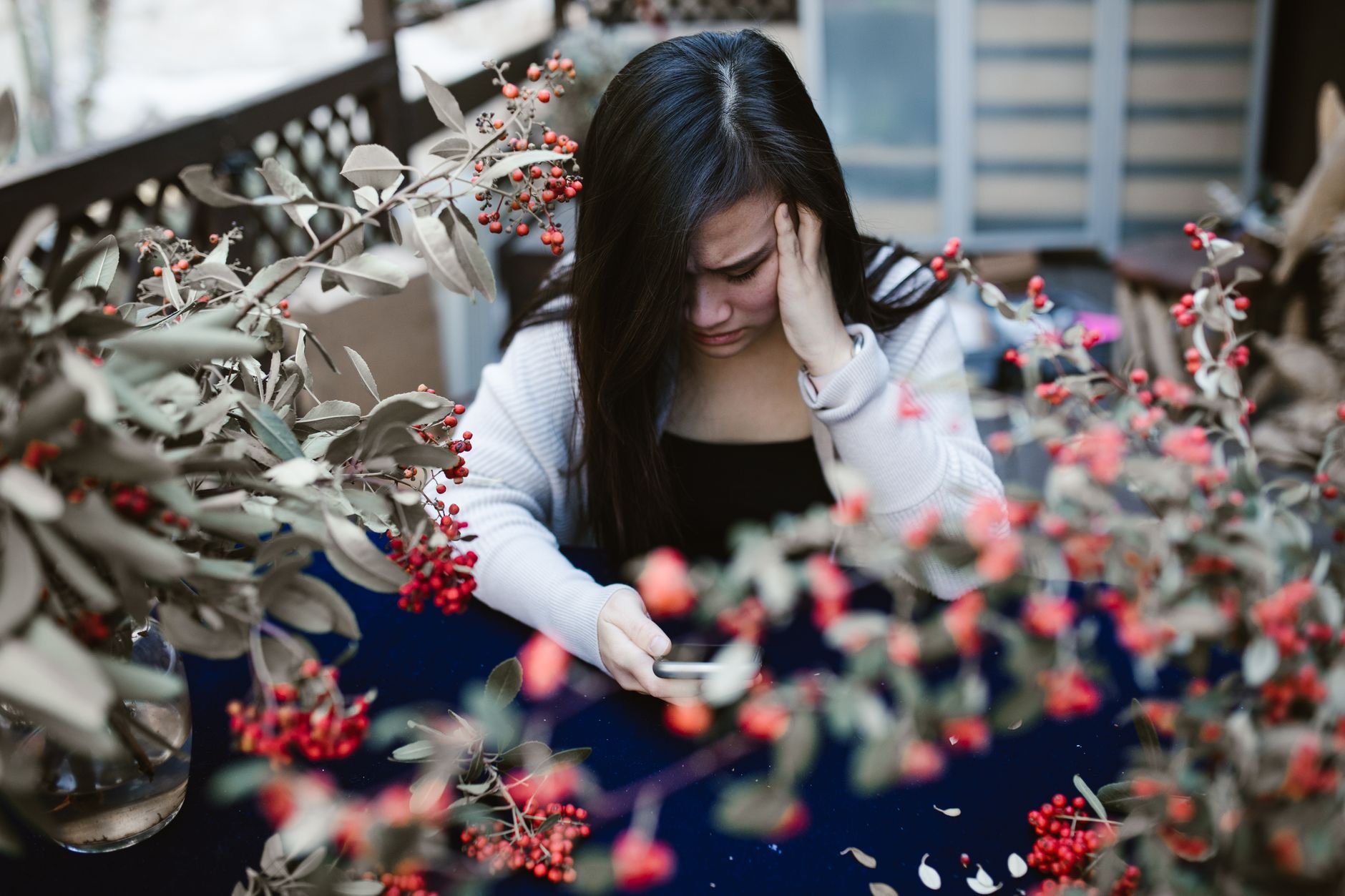 Woman in a dimly lit room looking at her smartphone with a worried expression, suggesting a disturbing message.