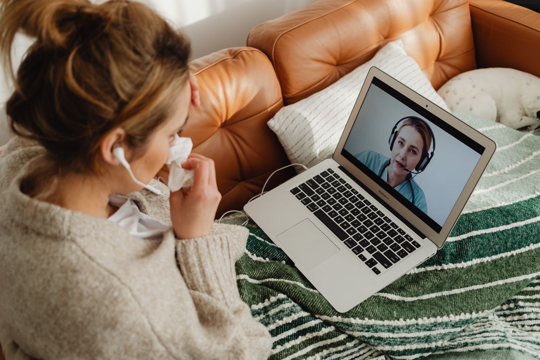 Person sitting on a couch during a video call with a supportive therapist, holding a cup of tea.