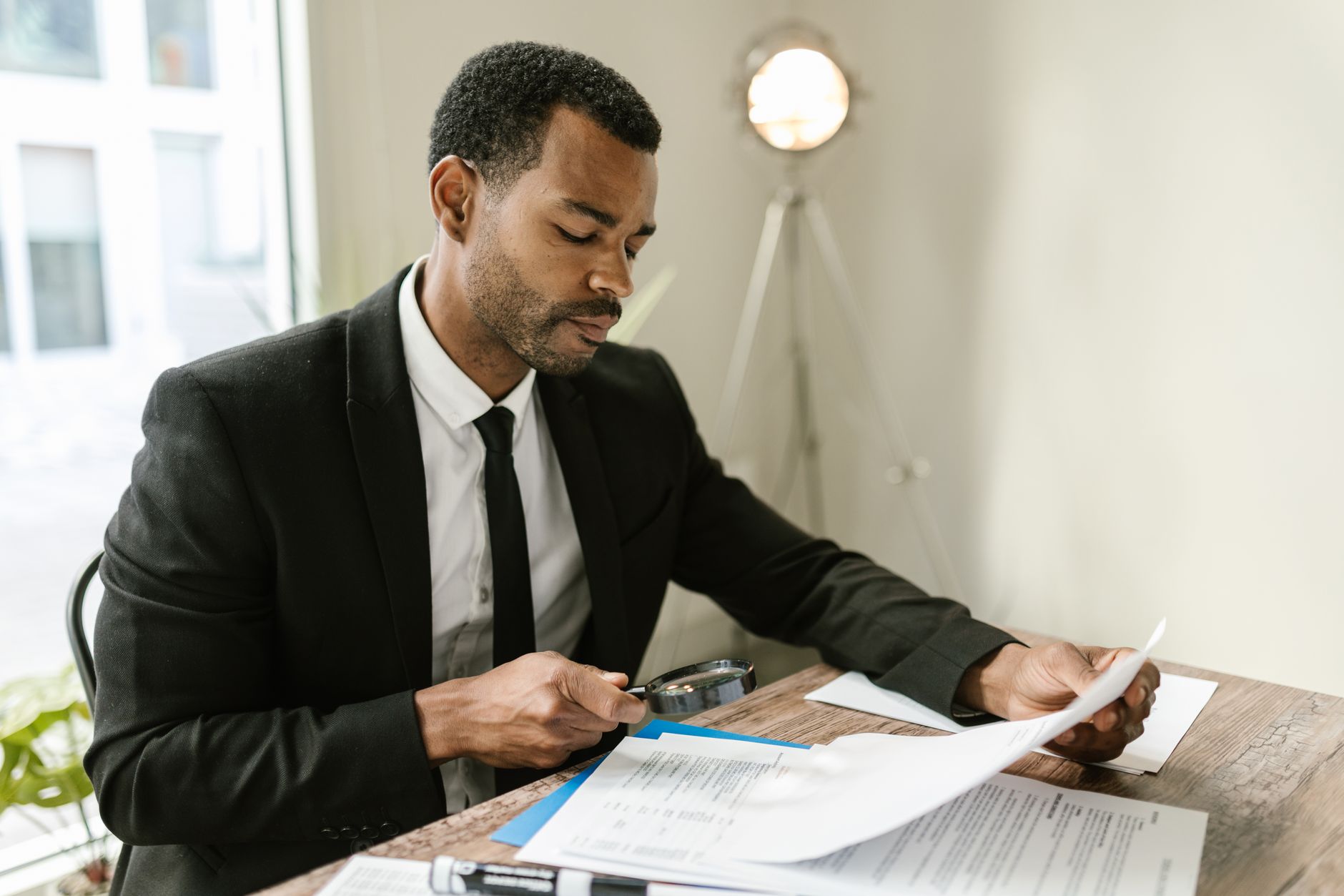 a person checking a legal document with a magnifying glass at a desk while using a laptop